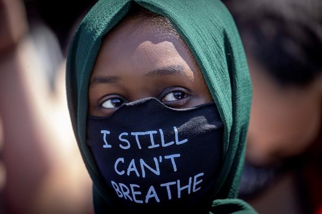 A person wears a mask Sunday, May 31, 2020, with a message at the Minneapolis corner where George Floyd was restrained by Minneapolis police. Floyd died May 25 after he was pinned at the neck by a Minneapolis police officer. (Elizabeth Flores/Star Tribune via AP)