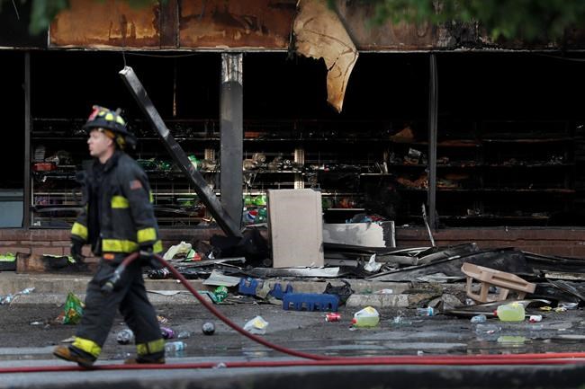 A member of the St. Louis Fire Department wraps up their work outside a vandalized and burned convenience store, Tuesday, June 2, 2020, in St. Louis. On Monday night people were seen removing items from the store before the building went up in flames and after a large peaceful protest against the death of George Floyd who died after being restrained by Minneapolis police officers on May 25 had ended. (AP Photo/Jeff Roberson)