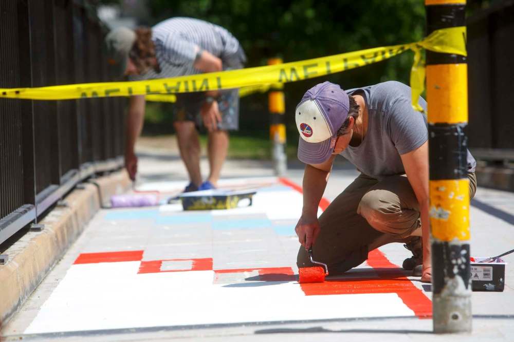 Artist Jamie Morneau (front) and Stéphane Dorge, organizer for Cool Streets Winnipeg, paint on a footbridge in Bunn’s Creek Centennial Park on Thursday. The two are realizing artist Nereo Zorro’s mural. (Mike Deal / Winnipeg Free Press)