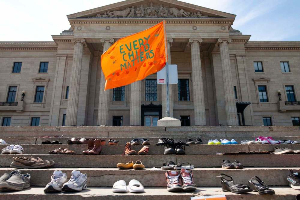 An orange flag with the words “every child matters” flies above the shoes that have been placed on the steps of the Manitoba legislature to honour of the children who died at residential school. (Daniel Crump / Winnipeg Free Press)