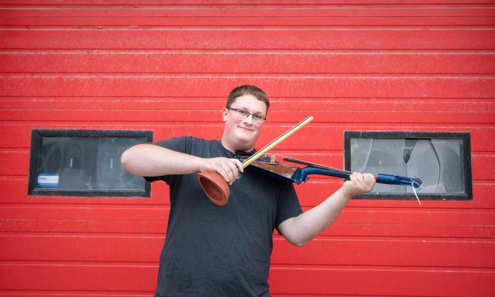 Jared Warkentin, assistant at St. Vital Museum, with a bow and fiddle made from a toilet plunger and shovel. (Jessica Lee / Winnipeg Free Press)