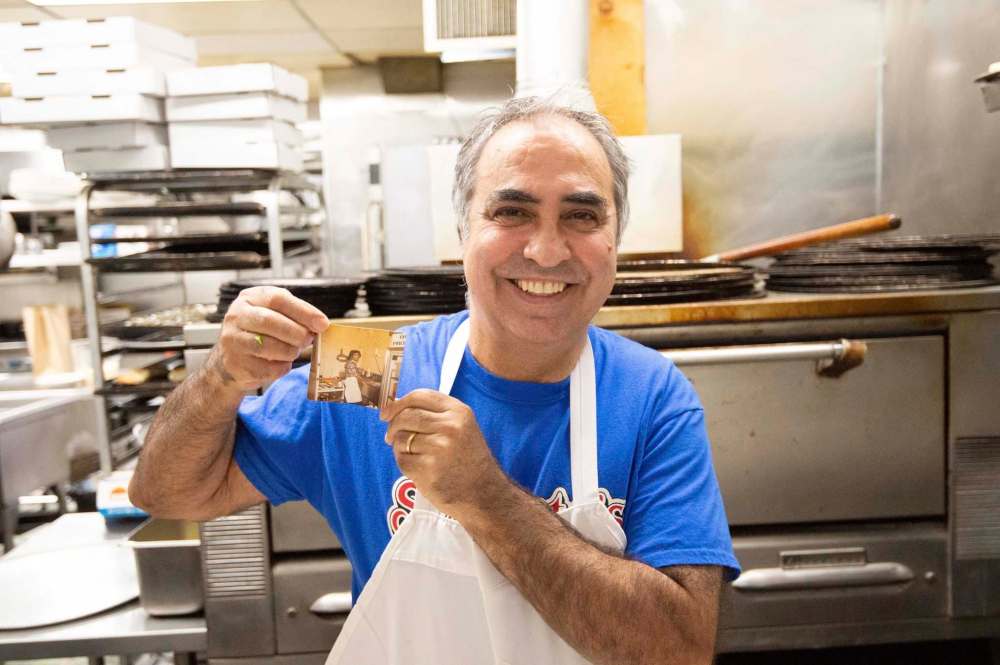Gerry Lomonaco, owner of Sorrento Pizza on Ellice Avenue, holds up a picture of himself working in the same kitchen he still works in 36 years later.