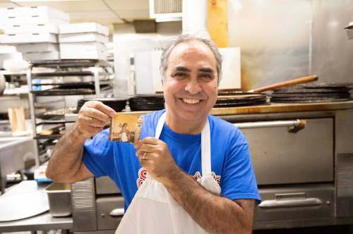 Gerry Lomonaco, owner of Sorrento Pizza on Ellice Avenue, holds up a picture of himself working in the same kitchen he still works in 36 years later.