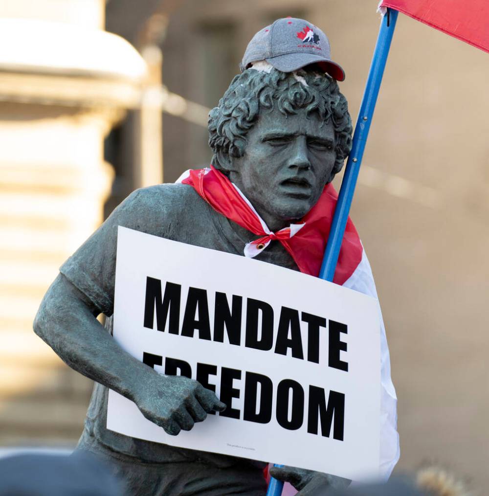 A statue of Terry Fox is decorated with a Canadian flag, protest sign and hat as protesters participating in a cross-country truck convoy protesting measures taken by authorities to curb the spread of COVID-19 and vaccine mandates walk gather Parliament Hill in Ottawa on Saturday, Jan. 29, 2022. THE CANADIAN PRESS/Adrian Wyld