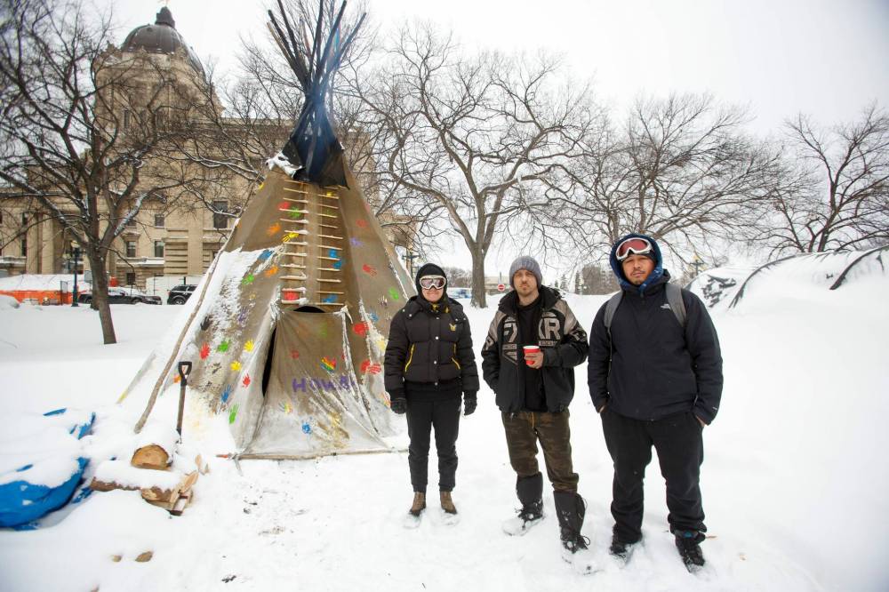 Volunteer fire keepers Holly Enns (left) with her partner Daniel “Kuya” Caneda (right) and full-time fire keeper John Butler (centre) keep watch over the sacred fire. (Mike Deal / Winnipeg Free Press)