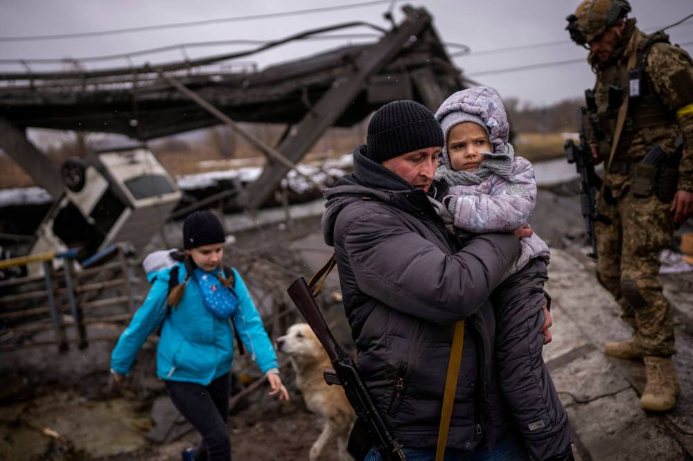 Local militiaman Valery, 37, carries a child as he helps a fleeing family across a bridge destroyed by artillery, on the outskirts of Kyiv, Ukraine, Wednesday, March 2. 2022. Russian forces have escalated their attacks on crowded cities in what Ukraine’s leader called a blatant campaign of terror. (Emilio Morenatti / The Associated Press)