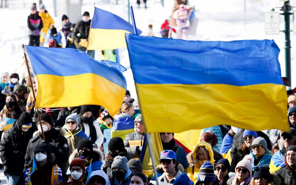 A row, flags of blue and yellow were hoisted along with protest placards at the rally. (John Woods / Winnipeg Free Press)