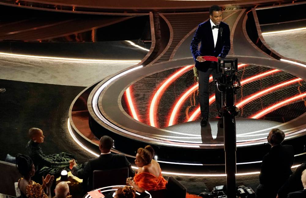 Chris Rock (right) speaks onstage as Jada Pinkett Smith and Will Smith (bottom left) look on after Smith went onstage and slapped Rock. (Chris Pizzello / The Associated Press)