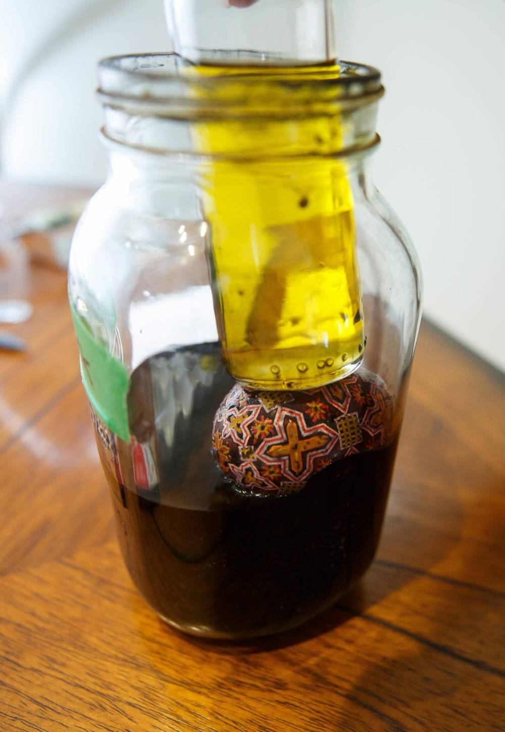 Rossier uses a small container of oil to hold down a pysanka in a jar of black dye.