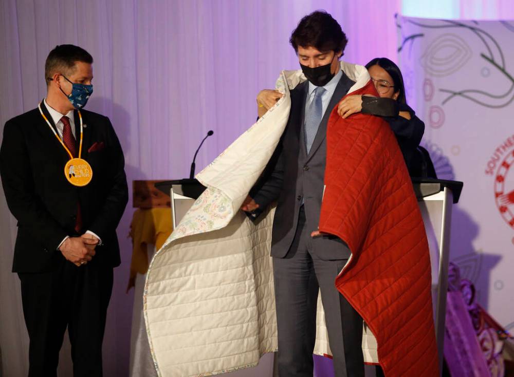 Southern Chiefs’ Organization gives a blanket to Prime Minister Justin Trudeau as Mayor Brian Bowman looks on at a Hudson’s Bay Company transfer ceremony in Winnipeg Friday, April 22, 2022. One of the landmark stores formerly run by the Hudson’s Bay Company is about to undergo a major transformation in the name of reconciliation with Indigenous people. THE CANADIAN PRESS/John Woods