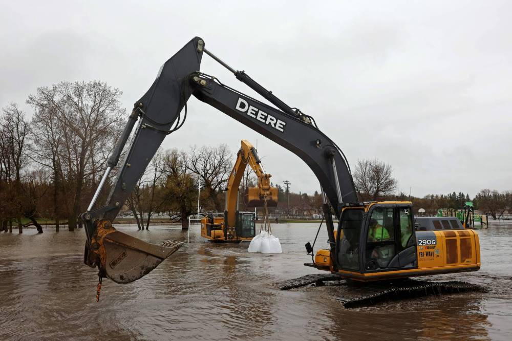 An excavator carries super sandbags through the rising floodwaters of the Little Saskatchewan River to create a dike to protect Minnedosa Collegiate. (Tim Smith / The Brandon Sun)