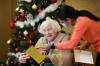 RUTH BONNEVILLE / WINNIPEG FREE PRESS Local - Convalescent Home Feature Convalescent Home of Winnipeg resident, Mildred Giesbrecht, 105 years old, enjoys opening her gifts from the home presented to her by staff, Sherry Heppner, development coordinator (red), and Kiran Benipal recreation manager (orange), in front of their Christmas tree in the home’s foyer this week. One of the gifts given to residents was a shawl which the staff tried on Mildred after it was opened. Photos for Christmas feature on how this PCH is adapting to their second pandemic Christmas. Sherry with gifts. Dec 21st, 2021