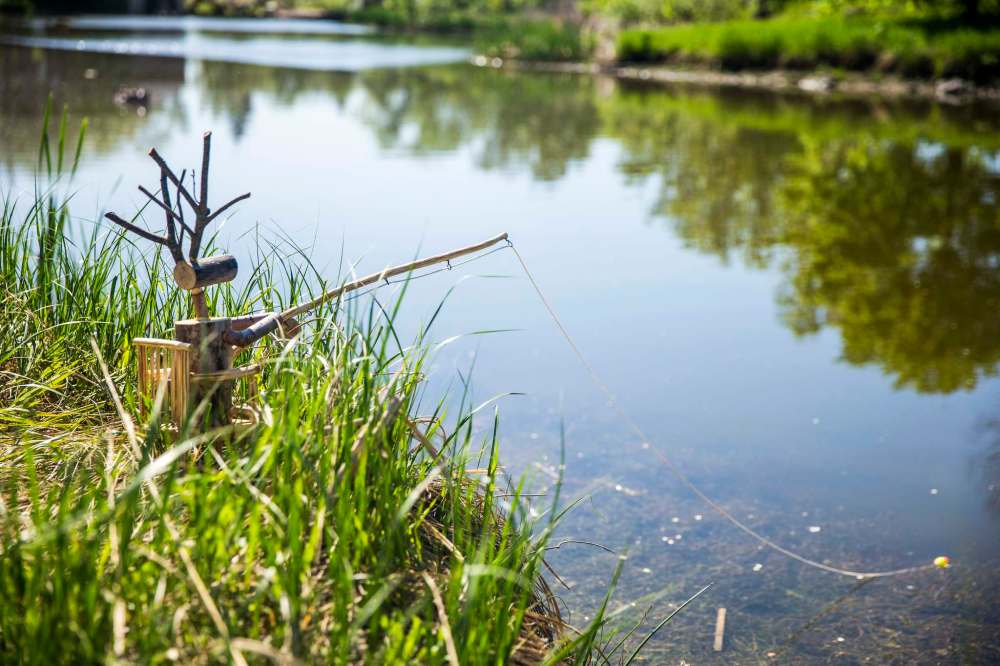 A reindeer sits in a chair beside Sturgeon Creek while fishing. Most of the sculptures are installed at ground level in bushes and beside trees, blending into the landscape. (Mikaela MacKenzie / Winnipeg Free Press)