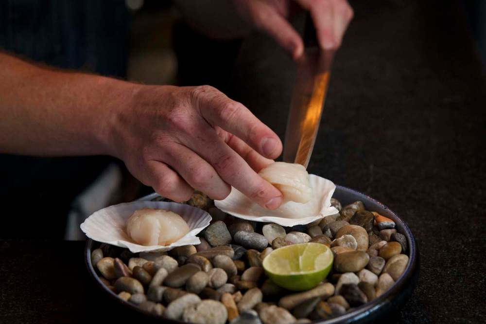 Dustin Pajak plates an order of scallops on the half shell, served with avocado, pumpkin seed and passion fruit purée. (Mike Deal / Winnipeg Free Press)