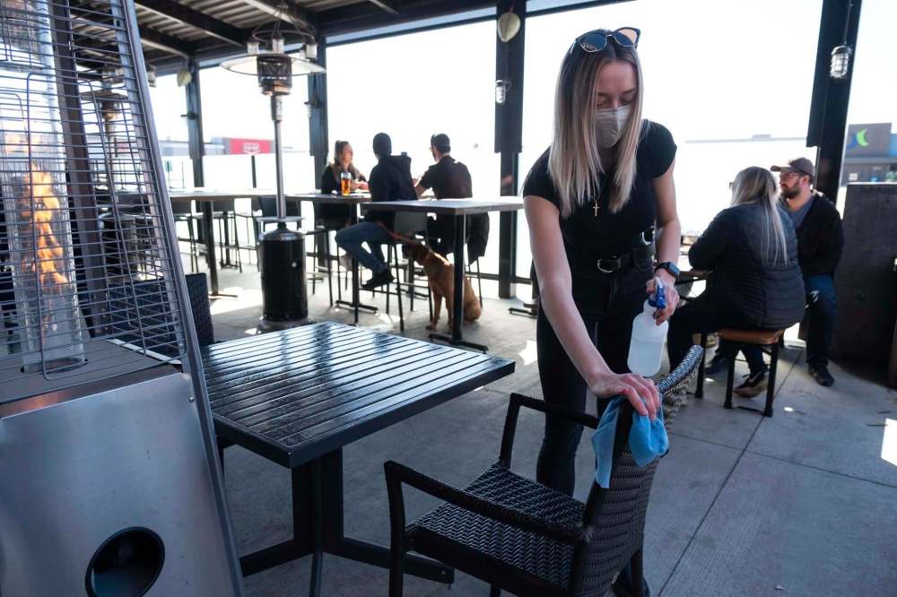 Jasmine Brown disinfects the table and chairs in preparation for seating guests on the patio at Fionns on Grant Avenue. (Daniel Crump / Winnipeg Free Press)