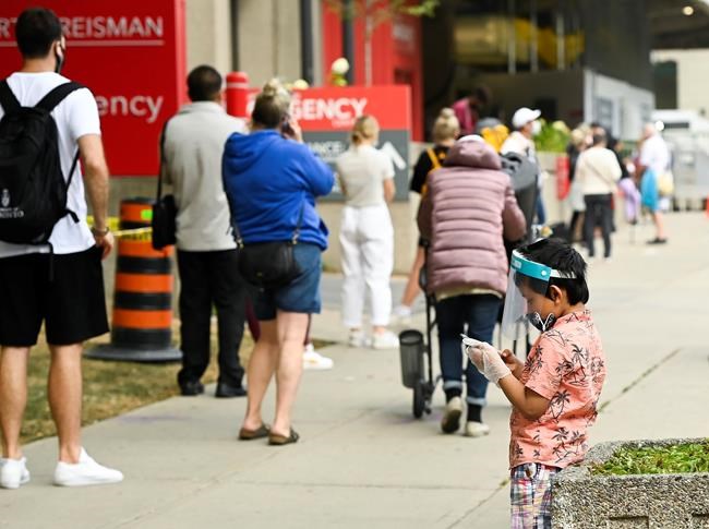 A young boy plays on a phone as he waits in line at a COVID assessment centre at Mount Sinai Hospital during the COVID-19 pandemic in Toronto on Thursday, September 24, 2020. THE CANADIAN PRESS/Nathan Denette