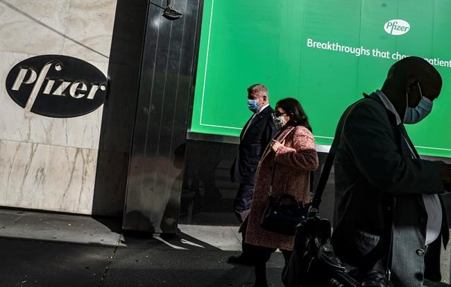 Pedestrians walk past Pfizer world headquarters in New York on Monday Nov. 9, 2020. Pfizer says an early peek at its vaccine data suggests the shots may be 90% effective at preventing COVID-19, but it doesn't mean a vaccine is imminent. (AP Photo/Bebeto Matthews)