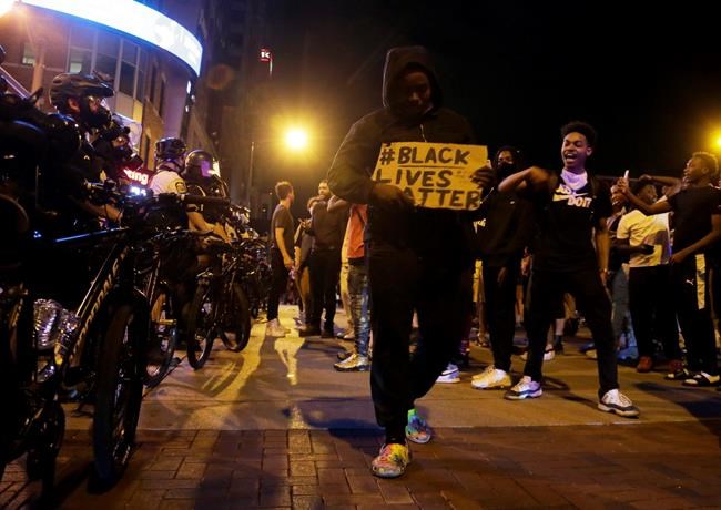 Protesters hold signs and walk past a line of police in downtown Columbus, Ohio, Thursday, May 28, 2020, during a demonstration over the death of George Floyd in police custody Monday in Minneapolis. Columbus police used pepper spray to disperse protesters after some threw plastic bottles of water, smoke bombs and other items at police. Windows at the Statehouse and in bus stations along High Street were shattered, trash cans were tossed and decorative planters wrecked. (Barbara J. Perenic/The Columbus Dispatch via AP)