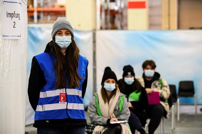 A woman representing medical personnel stands in front of sitting test persons in the waiting area in Mainz, Germany, Wednesday, Dec.2, 2020. The Minister of Health in Rhineland-Palatinate visited a trial vaccination centre. In order to test the structure, organisation and procedures with possible vaccinations against Covid-19, Rhineland-Palatinate has set up a trial vaccination centre in the state capital. (Andreas Arnold/dpa via AP)