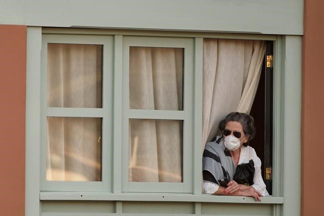A woman looks out of a window at the H10 Costa Adeje Palace hotel in La Caleta, in the Canary Island of Tenerife, Spain, Wednesday, Feb. 26, 2020. Spanish officials say a tourist hotel in Tenerife has been placed in quarantine after an Italian doctor staying there tested positive for the COVID-19 virus and Spanish news media says some 1,000 tourists staying at the complex are not allowed to leave. (AP Photo)