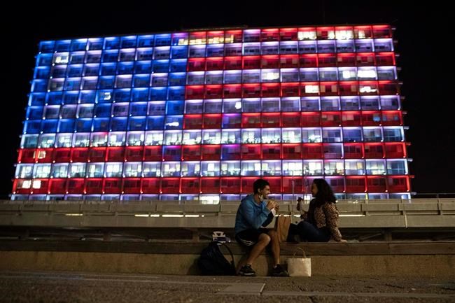 An Israeli couple sits near the Tel Aviv municipality building as it is lit up with the flag of the United States in Tel Aviv, Israel, Thursday, Jan. 7, 2021. Officials said the display is a sign of solidarity with the United States and support for democracy. (AP Photo/Sebastian Scheiner)