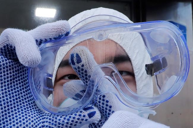 A worker cleans his goggles to spray disinfectant as a precaution against the coronavirus at a shopping street in Seoul, South Korea, Thursday, Feb. 27, 2020. South Korea and China each reported hundreds more virus cases Thursday as the new illness persists in the worst-hit areas and spreads beyond borders. (AP Photo/Ahn Young-joon)