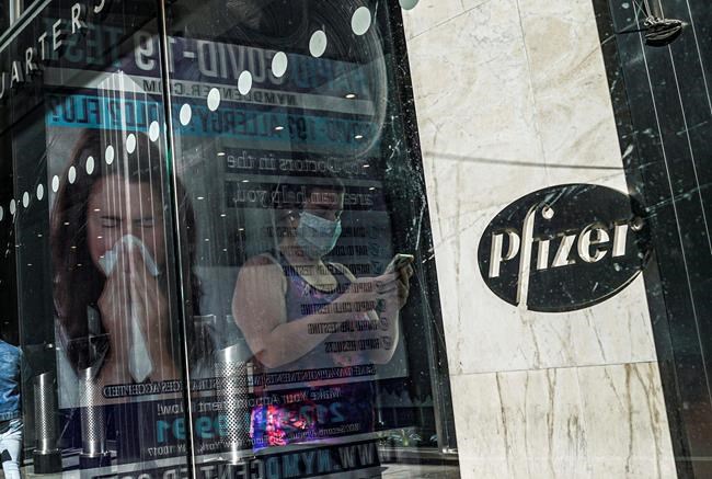 FILE - In this Nov. 9, 2020, file photo, an ad for COVID-19 testing reflects on glass at a bus stop, as pedestrians walk past Pfizer world headquarters in New York. Pfizer and BioNTech say they've won permission Wednesday, Dec. 2, 2020, for emergency use of their COVID-19 vaccine in Britain, the world’s first coronavirus shot that’s backed by rigorous science -- and a major step toward eventually ending the pandemic. (AP Photo/Bebeto Matthews, File)