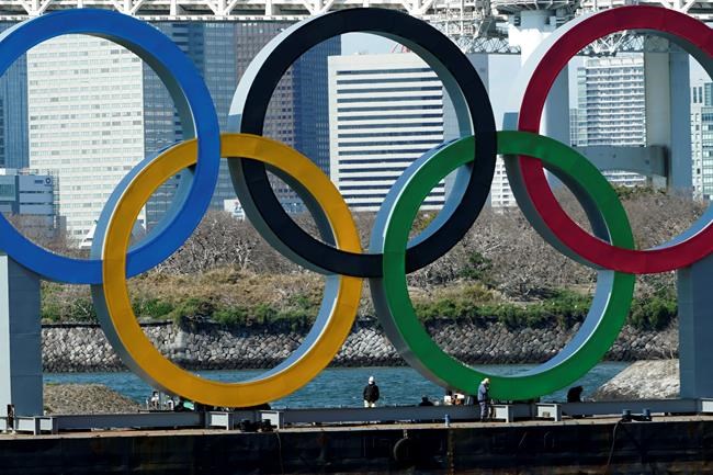 FILE - In this March 24, 2020, file photo, workers stand at the bottom of the Olympic rings at Tokyo's Odaiba district. Just two months after the unprecedented postponement. Chief Executive Toshiro Muto was asked Thursday, May 28, 2020 about progress rescheduling next year's Tokyo Olympics. (AP Photo/Eugene Hoshiko, File)