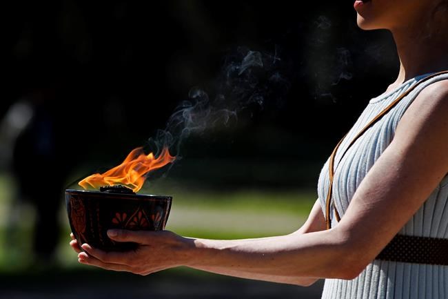 FILE - In this March 12, 2020, file photo, an actress, playing the role of the priestess, holds the flame during the flame lighting ceremony at the closed Ancient Olympia site, birthplace of the ancient Olympics in southern Greece. The Olympic flame from Greece is set to arrive in Japan even as the opening of the the Tokyo Games in four months is in doubt with more voices suggesting the games should to be postponed or canceled because of the worldwide virus pandemic. (AP Photo/Thanassis Stavrakis, File)