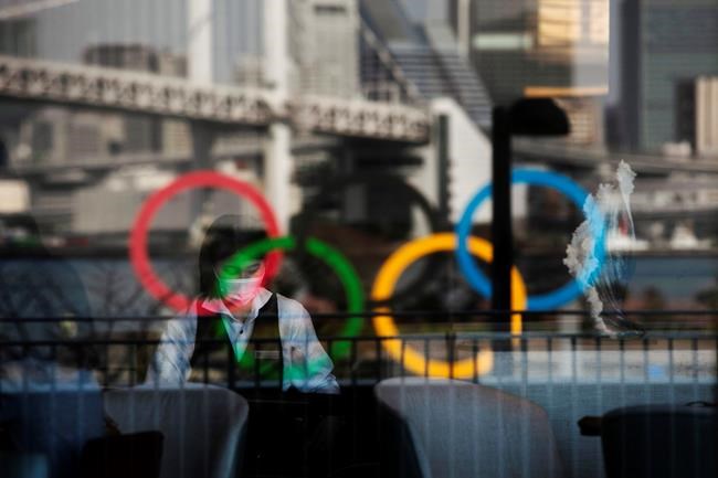 FILE - In this Feb. 24, 2020, photo, the Olympics rings are reflected on the window of a hotel restaurant as a server with a mask sets up a table, in the Odaiba section of Tokyo. The vaccine rollout in Japan has been very slow with less than 1% vaccinated. This of course is spilling over to concerns about the postponed Tokyo Olympics that open in just over three months.(AP Photo/Jae C. Hong, File)