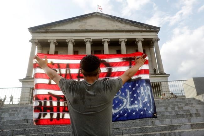 A man holds a flag upside down in front of the State Capitol during a peaceful protest Thursday, June 4, 2020, in Nashville, Tenn., over the death of George Floyd, who died May 25 after being restrained by police in Minneapolis. (AP Photo/Mark Humphrey)