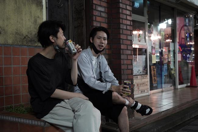 Naoto Suga, right, 25, drinks canned alcohol roadside with his friend in Tokyo’s Shinjuku district Monday, July 19, 2021.