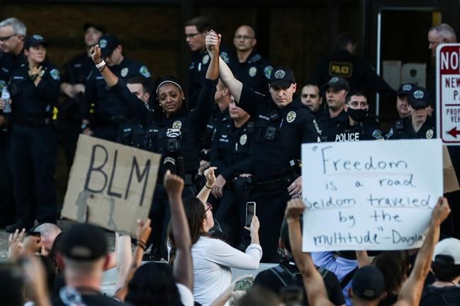 APD officer Alexandra Parker holds her hand up with a fellow officer as they kneel together with protesters at the Austin Police Department HQ during a Black Lives Matter rally in Austin on Thursday, June 4, 2020. (Lola Gomez/Austin American-Statesman via AP)