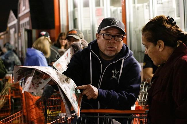 Jorge and Jo Ann Delgadillo examine a Home Depot coupon insert for the Black Friday deals while they wait the final half hour before the store opens at 6 a.m. on Friday, Nov. 29, 2019, in Brownsville, Texas. (Denise Cathey/The Brownsville Herald via AP)