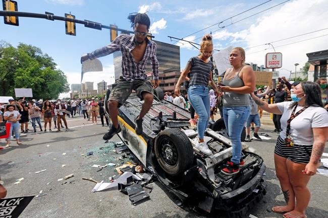 FILE - in this Saturday, May 30, 2020 file photo, protesters climb on a flipped over police vehicle, in Salt Lake City. Protests in Salt Lake City that drew several thousand people are a setback for contact tracers already struggling to contain the spread of the coronavirus, said Tair Kiphibane, infectious disease bureau manager for the Salt Lake County Health Department. (AP Photo/Rick Bowmer, File)