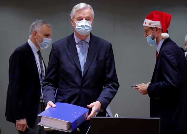 A collegue wears a Christmas hat as European Union chief negotiator Michel Barnier, center, carries a binder of the Brexit trade deal during a special meeting of Coreper, at the European Council building in Brussels, Friday, Dec. 25, 2020. European Union ambassadors convened on Christmas Day to start an assessment of the massive free-trade deal the EU struck with Britain. After the deal was announced on Thursday, EU nations already showed support for the outcome and it was expected that they would unanimously back the agreement, a prerequisite for its legal approval. (Olivier Hoslet, Pool via AP)