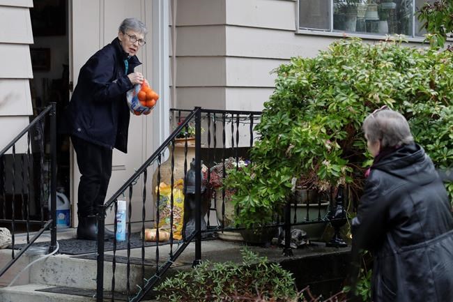 Pat McCauley gathers groceries and other items left on her porch by her daughter, Cheri Chandler, right, at her home, Friday, March 6, 2020, in Kirkland, Wash. Pat and her husband Bob have been self-quarantined in their home during the past week due to having visited friends at the Life Care Center nursing home — which has become the epicenter of the outbreak of the COVID-19 coronavirus in Washington state — several times in February. (AP Photo/Ted S. Warren)