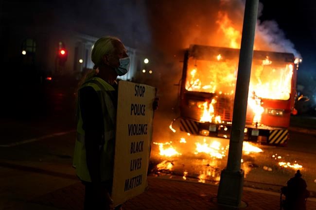 A protester stands near a burning garbage truck outside the Kenosha County Courthouse, late Monday, Aug. 24, 2020, in Kenosha, Wis. Protesters converged on the county courthouse during a second night of clashes after the police shooting of Jacob Blake a day earlier turned Kenosha into the nation’s latest flashpoint city in a summer of racial unrest. (AP Photo/David Goldman)