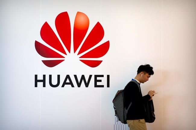 FILE - In this Oct. 31, 2019, file photo, a man uses his smartphone as he stands near a billboard for Chinese technology firm Huawei at the PT Expo in Beijing. The Justice Department has added new criminal charges against Chinese tech giant Huawei and two of its United States subsidiaries, accusing the company in a plot to steal trade secrets. The indictment from federal prosecutors was announced Thursday by federal prosecutors in Brooklyn. (AP Photo/Mark Schiefelbein, File)