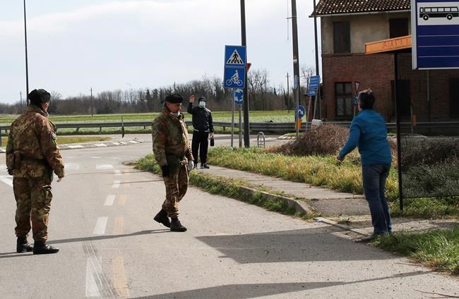 A woman outside the cordoned area salutes a man inside, after leaving on a bench at the bus stop some goods for him, at a checkpoint in Turano Lodigiano, Italy, Wednesday, Feb. 26, 2020. The viral outbreak that began in China and has infected more than 80,000 people globally, so far caused 374 cases and 12 deaths in Italy, according to the last numbers released by civil protection. (AP Photo/Antonio Calanni)