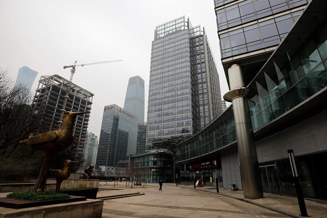 A woman wearing a protective face mask walks alone at a quiet office buildings compound in Beijing, Monday, Feb. 24, 2020. Regulators on Monday promised tax cuts and other aid to help companies recover from China's virus outbreak and expressed confidence the ruling Communist Party's growth targets can be achieved despite anti-disease controls that shut down much of the economy. (AP Photo/Andy Wong)
