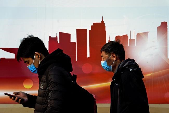 People wearing face masks to help curb the spread of the coronavirus walk by a moral depicting China's skyscrapers along a street in Beijing, Sunday, Dec. 6, 2020. Provincial governments across China are placing orders for experimental, domestically made coronavirus vaccines, though health officials have yet to say how well they work or how they may reach the country's 1.4 billion people. (AP Photo/Andy Wong)