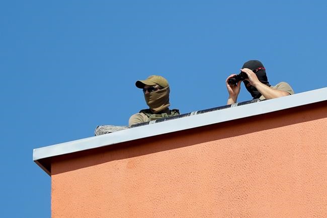 Belarusian Interior Ministry soldiers watch from a ruff as friends and relatives of those detained during mass rally following presidential election gather at a detention center in Minsk, Belarus, Tuesday, Aug. 11, 2020. The Belarusian Interior Ministry said Tuesday that more than 2,000 people were detained across the country for taking part in unsanctioned protests on Monday evening and overnight. It added that 21 police officers were injured in clashes with protesters, and five of them were hospitalized. (AP Photo/Sergei Grits)