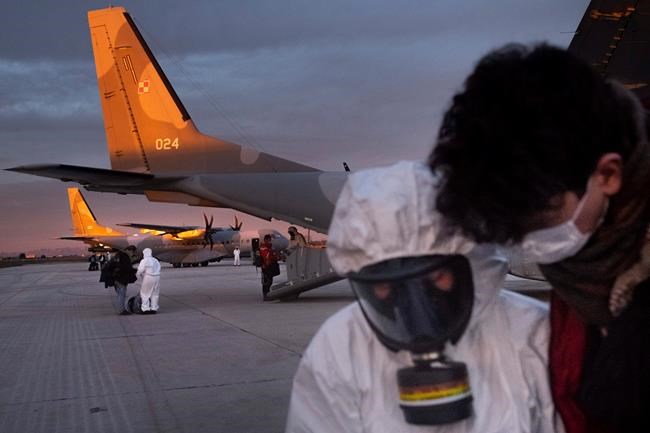 In this Feb. 2, 2020, photo, Polish military personnel wearing protective suits talk with evacuees from Wuhan, China, after their arrival at an airport in Marseilles, France. China said Tuesday the number of infections from a new virus surpassed 20,000 as medical workers and patients arrived at a new hospital and President Xi Jinping said