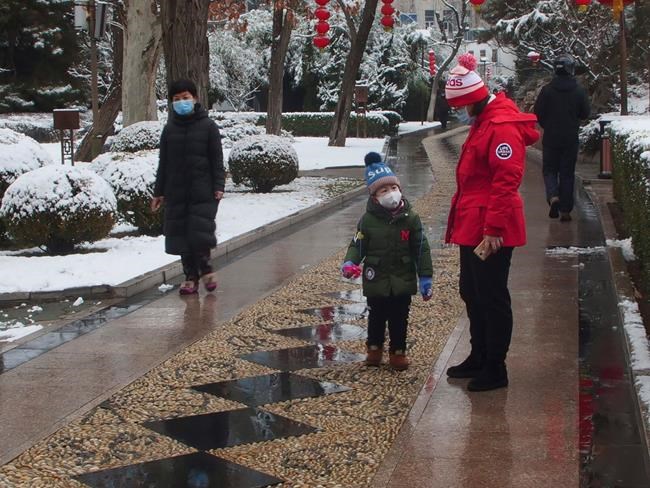 People wear face masks as they walk in public park on a snowy day in Beijing, Sunday, Feb. 2, 2020. The Philippines on Sunday reported the first death from a new virus outside of China, where authorities delayed the opening of schools in the worst-hit province and tightened quarantine measures in a city that allow only one family member to venture out to buy supplies. (Miriam Saleh via AP)