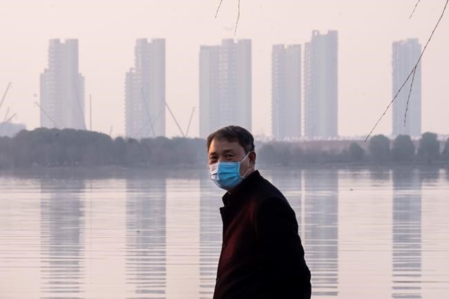 A man wears a face mask as he stands along the waterfront in Wuhan in central China's Hubei Province, Thursday, Jan. 30, 2020. China counted 170 deaths from a new virus Thursday and more countries reported infections, including some spread locally, as foreign evacuees from China's worst-hit region returned home to medical observation and even isolation. (AP Photo/Arek Rataj)