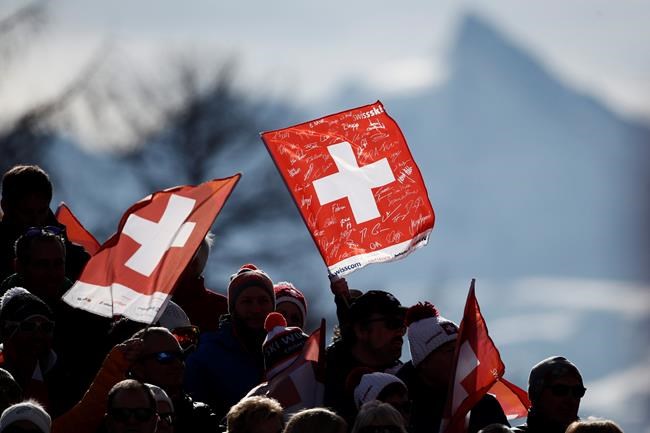 Fans wave Swiss flags at the finish area of an alpine ski, women's World Cup downhill, in Crans Montana, Switzerland, Friday, Feb. 21, 2020. (AP Photo/Gabriele Facciotti)