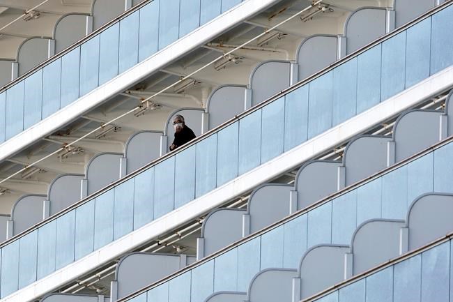 A passenger stand outside on the balcony of the cruise ship Diamond Princess anchored at the Yokohama Port Thursday, Feb. 6, 2020, in Yokohama, near Tokyo. The 3,700 people on board faced a two-week quarantine in their cabins. Health workers said 10 more people from the Diamond Princess were confirmed sickened with the virus, in addition to 10 others who tested positive on Wednesday. The 10 will be dropped off as the ship docks and transferred to nearby hospitals for further test and treatment. (AP Photo/Eugene Hoshiko)