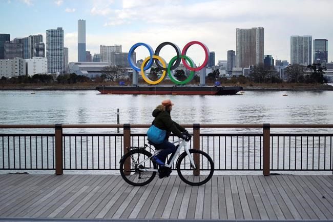 A man rides a bicycle near the Olympic rings floating in the water in the Odaiba section Friday, Jan. 8, 2021 in Tokyo. The senior member of the International Olympic Committee has said he “can’t be certain”the postponed Tokyo Olympics will open in just over six months because of the surging pandemic in Japan and elsewhere. (AP Photo/Eugene Hoshiko)