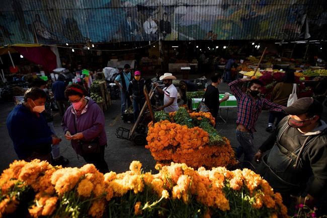 Customers, wearing protective face masks amid the new cornavirus pandemic, shop for flowers at the Jamaica Market, in Mexico City, Thursday, Oct. 29, 2020. Mexico’s Day of the Dead celebration this weekend won’t be the same in a year so marked by death, in a country where more than 90,000 people have died of COVID-19. Many of those had to be cremated rather than buried, and even for those with gravesides to visit, the pandemic has forced authorities in most parts of Mexico to close cemeteries to prevent the traditional Nov. 1-2 observances when entire families clean and decorate tombs. (AP Photo/Fernando Llano)